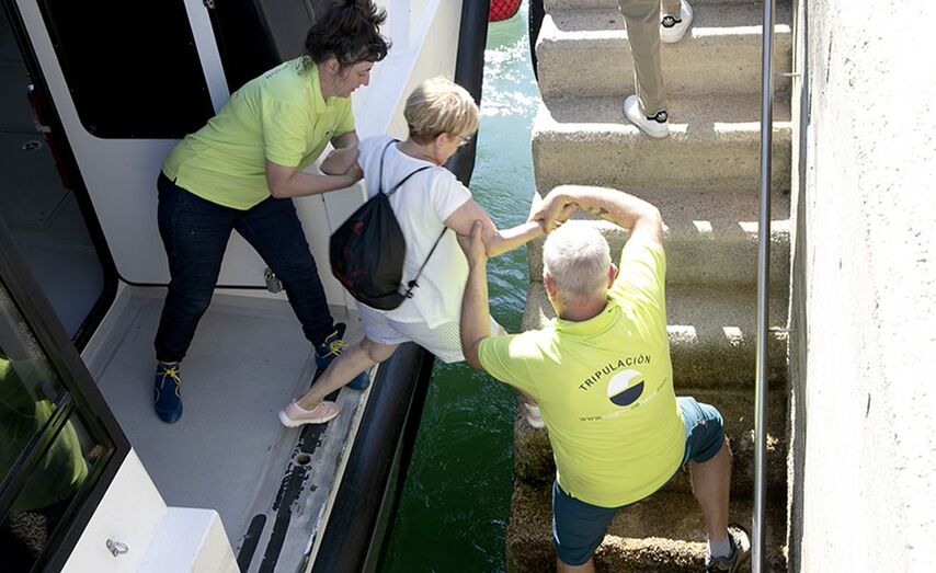Dos tripulantes de Nabia, esta misma ma&ntilde;ana, ayudan a una pasajera a saltar desde el muelle de piedra de Cangas al barco de Nabia.